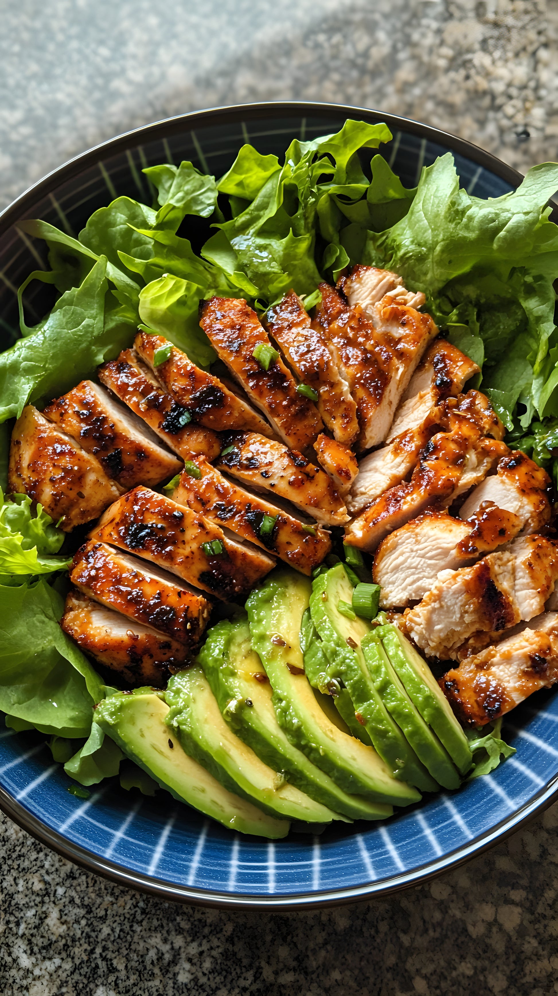 Grilled chicken breast seasoned with SwissAm Broil & Sauté, served with avocado slices on a bed of lettuce in a blue bowl.
